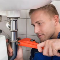 Young Male Plumber Fixing Sink In Kitchen